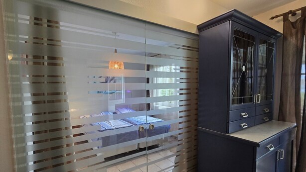 A bedroom with a bed, a dark cabinet with drawers, and a frosted glass partition. - Bungalow in Schlowe Am See (Borkow)