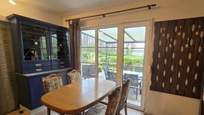 A dining area with a wooden table and chairs, a blue cabinet with glass doors, and a view of the outdoors through a glass door. - Bungalow in Schlowe Am See (Borkow)