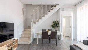 Uma sala de estar moderna com escada, área de jantar e TV sobre um suporte de madeira.