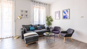 Uma sala de estar moderna com um sofá cinzento, duas poltronas, uma mesa de centro e um abajur. Há duas molduras na parede e um vaso com planta.