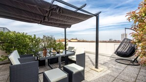 Um terraço no telhado com mesa, cadeiras e uma cadeira suspensa, com vista para o horizonte da cidade.
