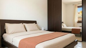 Une chambre à coucher avec un grand lit, une table de chevet et une vue sur une autre pièce, visible à travers une porte.