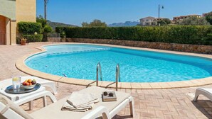 Une piscine bordée de pierres, des chaises longues et une table avec des fruits et un verre d’eau.