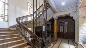 A grand staircase with ornate metal railings and a wooden handrail, leading to a dark wooden door with intricate patterns. - Downtown Glass & Glory Heritage Stay (Cairo)
