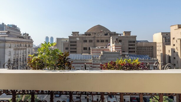 A balcony with a patterned floor, a decorative metal railing, and a view of a building with a dome and solar panels. - Downtown Glass & Glory Heritage Stay (Cairo)