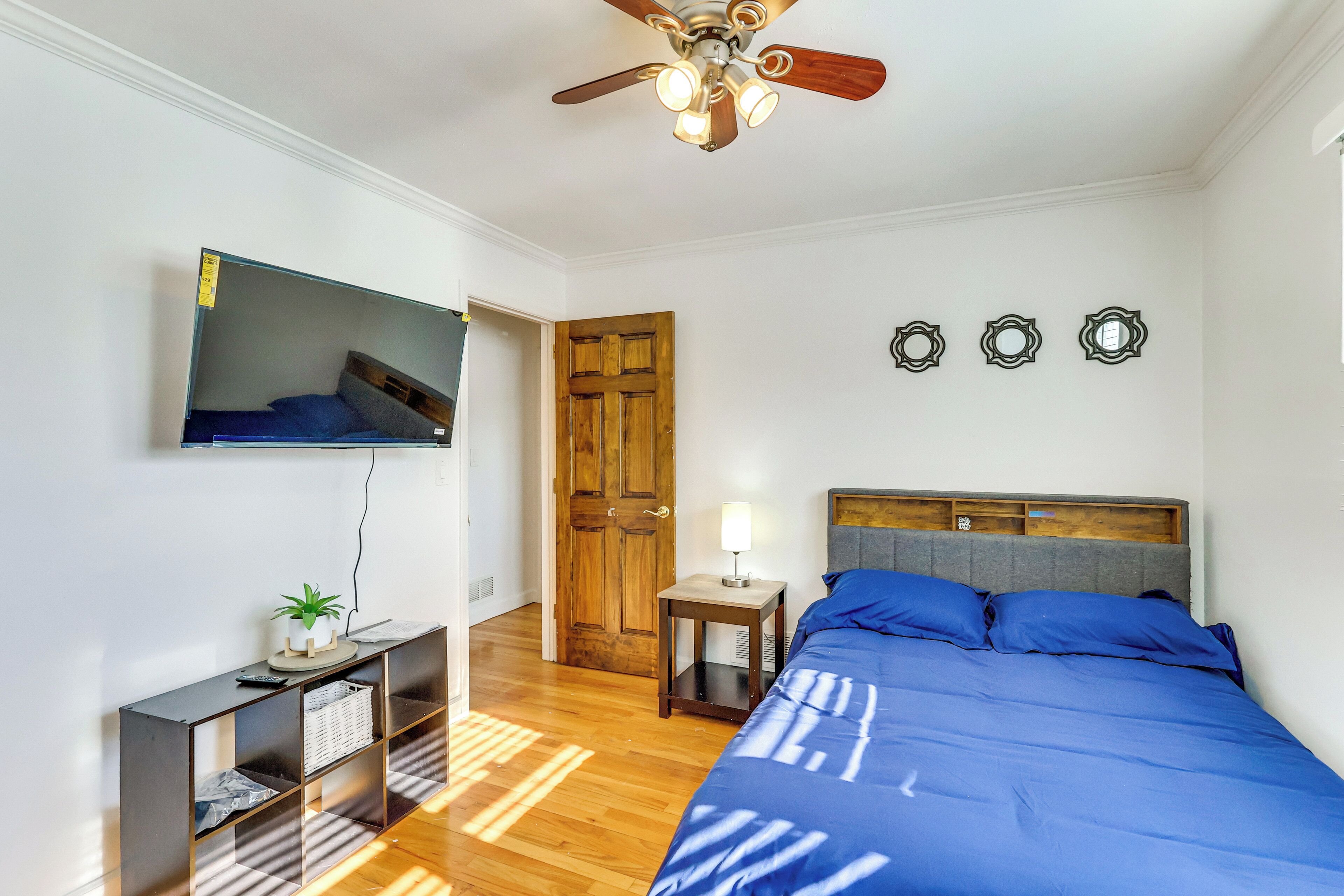 A bedroom with a bed, a TV mounted on the wall, a ceiling fan, and a wooden door.