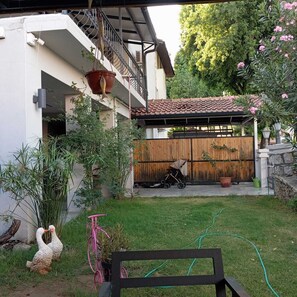 En lukket baghave med en delvist overdækket terrasse, et træhegn og forskellige planter.