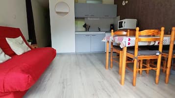 Un espacio habitable compacto con un sofá rojo, una mesa de comedor con sillas, una zona de cocina y un espejo redondo pequeño.