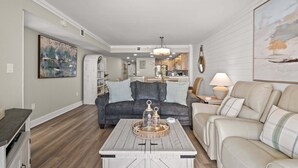 Ein Wohnzimmer mit grauem Sofa, beigem Sofa, Couchtisch mit Dekoration und einem Gemälde an der Wand.