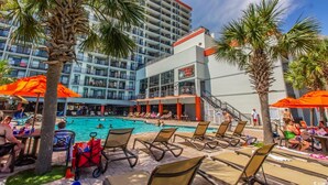 Ein Hotelpoolbereich mit Liegestühlen, Sonnenschirmen und Palmen.