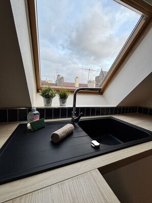 Cozinha com bancada preta, pia e janela com vista para a paisagem urbana.