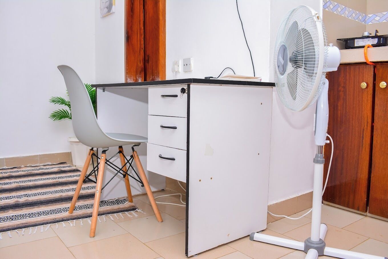 A compact office space with a white desk, a grey chair, and a standing fan.