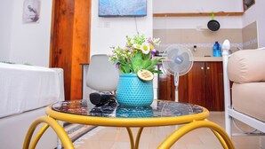 A living room with a round yellow table, a blue vase with flowers, a TV on the wall, and a wooden door. - Marve 408 Stylish Studio Apartment (Mtwapa)