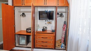 A walk-in closet with wooden cabinets, a television, a coffee maker, and a small refrigerator. - Standard Room in Gigiri near UN Nairobi, Cozy Stead Garden House (Nairobi)