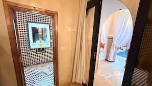 Hotellihuone, jossa on ruutukuviollinen lattia, geometrisesti kuvioitu peili ja näkymä uima-allasalueelle, jonka ikkunoissa on laskeutuvat verhot.