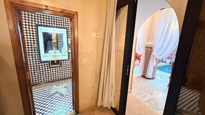 Hotellihuone, jossa on ruutukuviollinen lattia, mustavalkoinen kuvioitu peili ja näkymä uima-allasalueelle, jonka yllä on valkoinen katos.