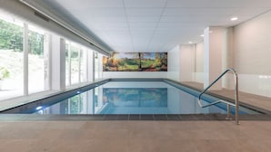 Una piscina interior con vistas a un área ajardinada, un mural en la pared y una barandilla de metal.