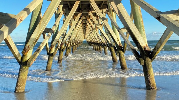 Una estructura de muelle de madera que se adentra en el océano, bajo un cielo despejado.