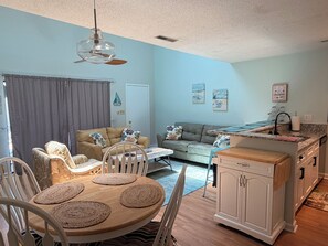 Ein Wohnzimmer mit Sofa, Sesseln, einem Esstisch und einer Küchenzeile mit Spüle und Schränken.
