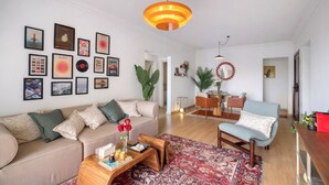 A modern living room with a sofa, coffee table, and a dining area with a chandelier.