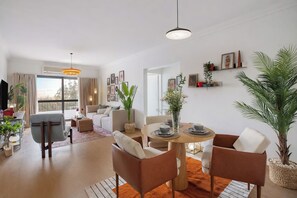 A modern living room with a dining area, a sofa set, and a large window with curtains.