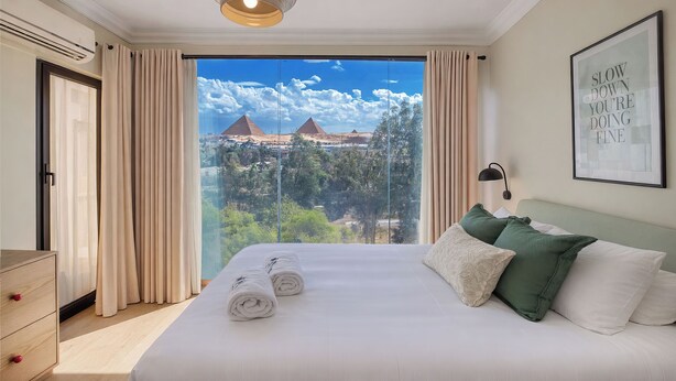 A hotel room with a large bed, a view of pyramids, and a motivational quote on the wall.