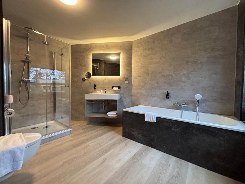 Een moderne badkamer met een douchecabine van glas, een vrijstaand bad en een wastafel met spiegel.