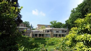 A building with a flat roof, multiple windows, and a lawn in the foreground. - Scenic Room Near Nijmegen Perfect for Family Adventures! Indoor Pool, Parking! (Berg en Dal)