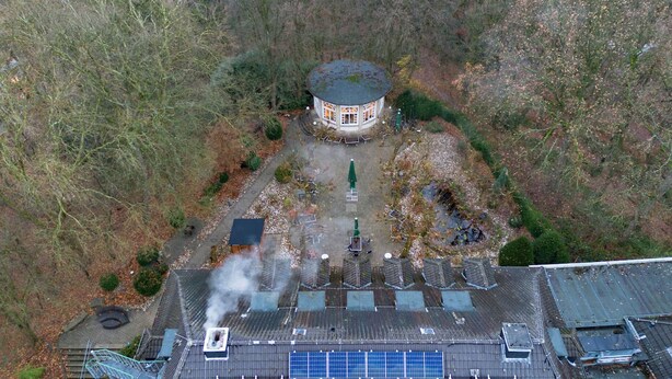 Luchtbeeld van een gebouw met een ronde constructie, omringd door een tuin met paden en zitplekken.
