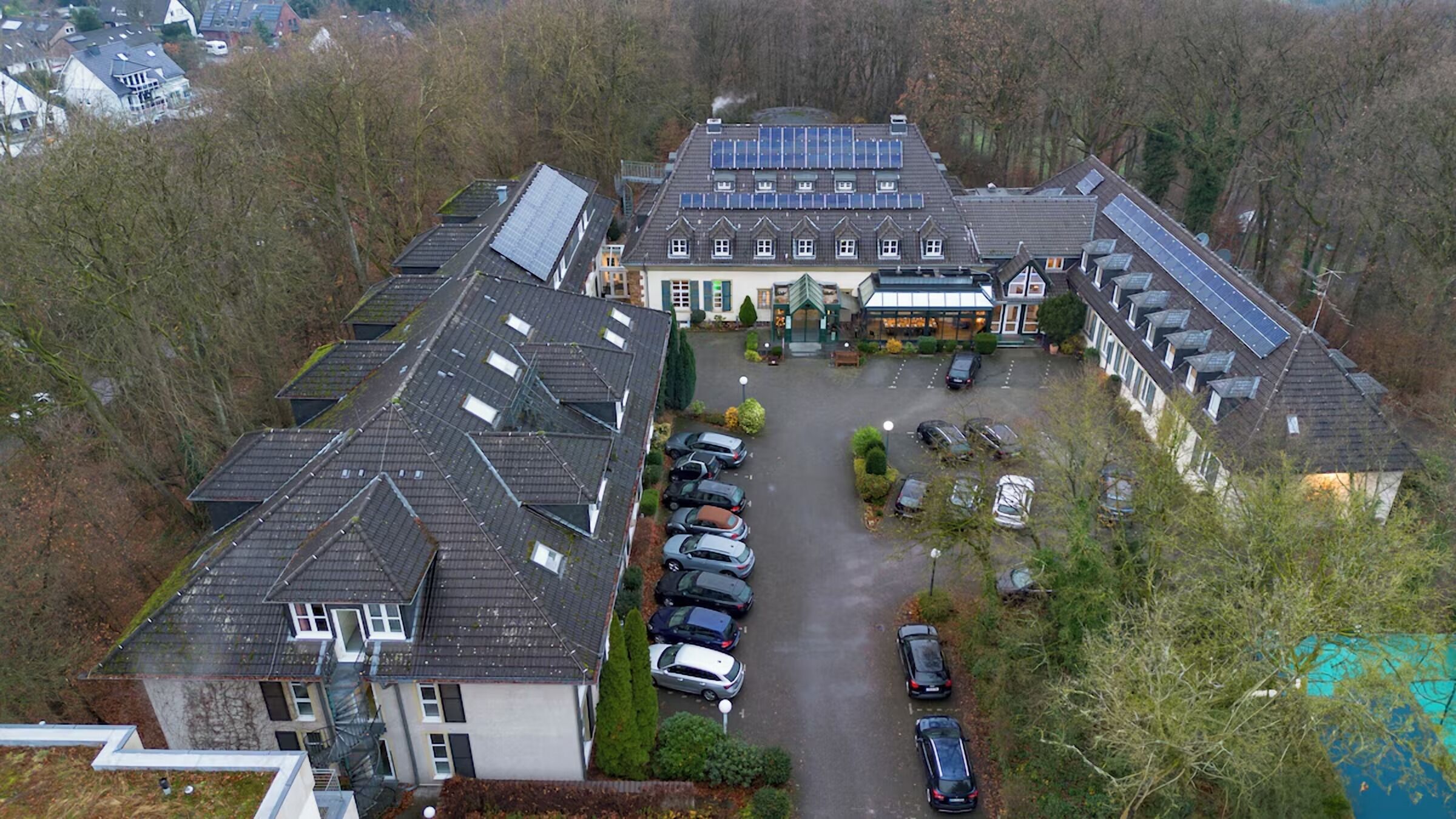 En boligbygning med solpaneler på taget, en parkeringsplads med flere biler og et lille haveareal.