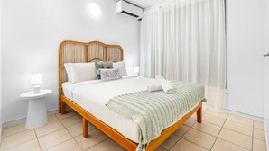 A neatly arranged bedroom with a wooden bed, a bedside table, an air conditioning unit, and a window with curtains. - Zen Bamboo Cozy - Modern - Central (Darwin)