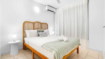 A neatly arranged bedroom with a wooden bed, a bedside table, an air conditioning unit, and a window with curtains.