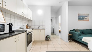 A modern kitchen with white cabinets, a stove, and a microwave. There is a small stool and a green sofa in the living area. - Zen Bamboo Cozy - Modern - Central (Darwin)
