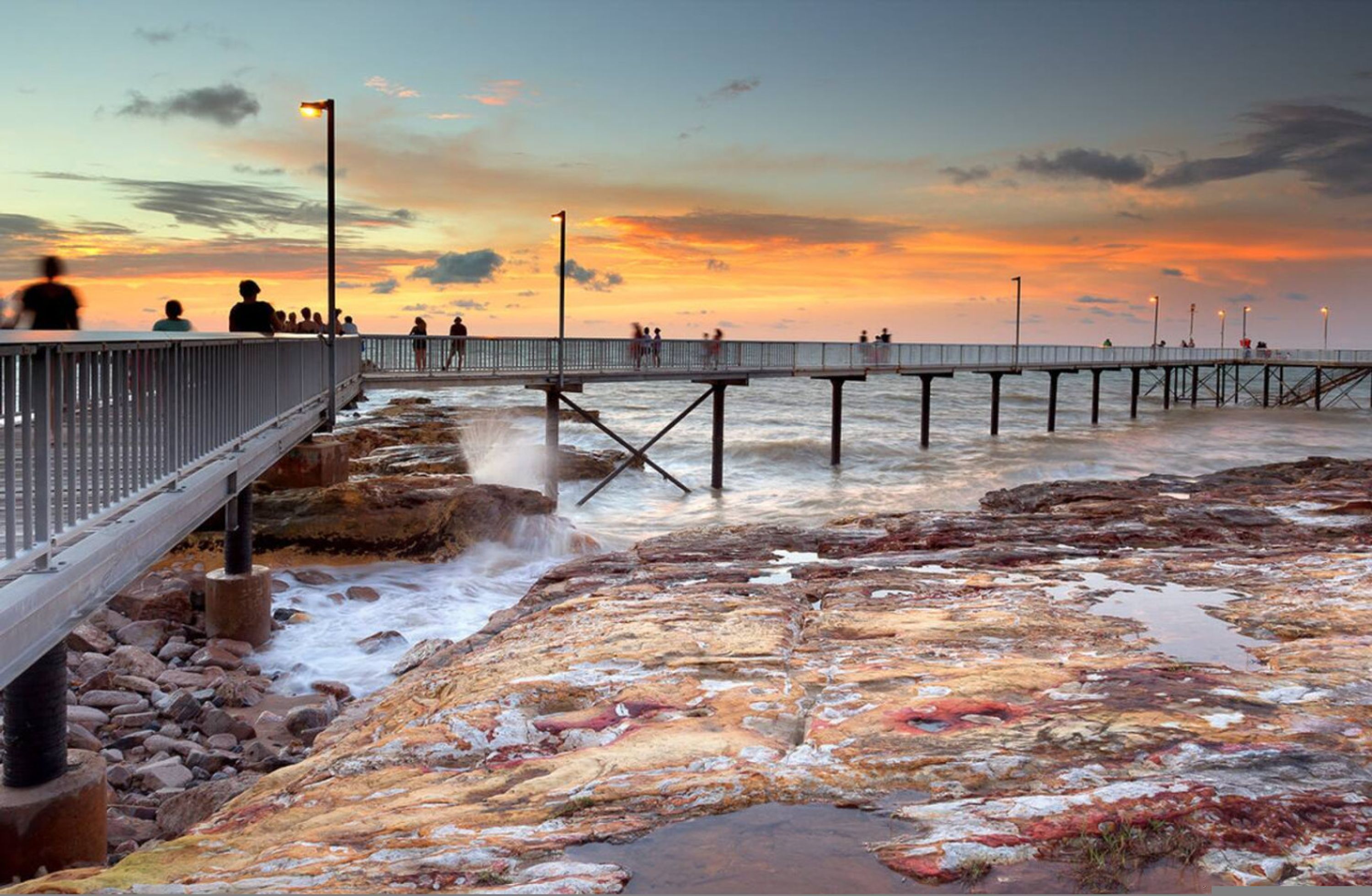 A pier extending into a rocky shoreline with a sunset in the background.