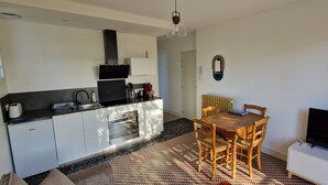 A compact kitchen with modern appliances, a dining area with a wooden table and chairs, and a flat-screen TV on a white cabinet. - Appartement "2" Villa Cây Tre Classé 3* (Rochefort)
