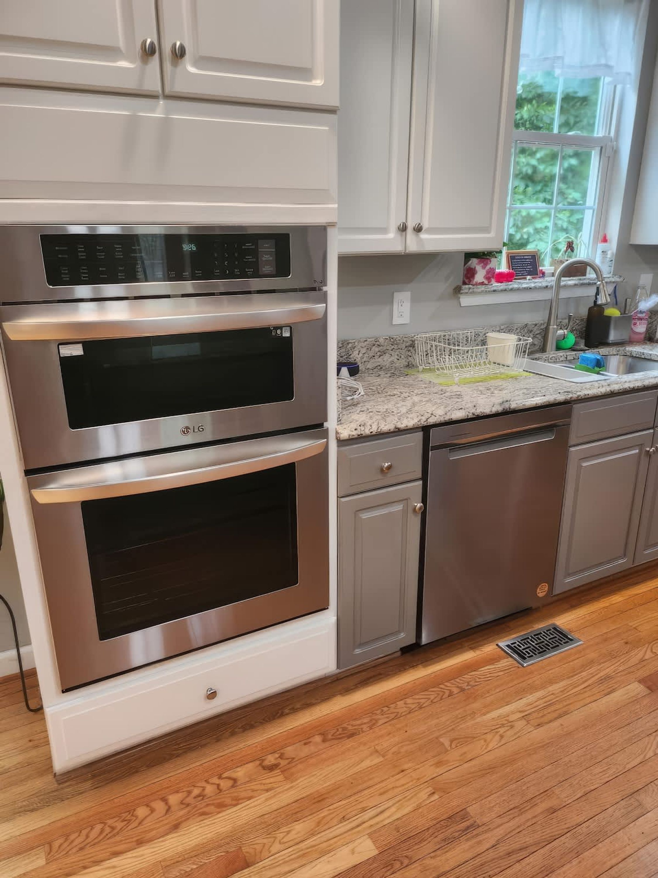 A kitchen with stainless steel appliances, white cabinetry, a granite countertop, and a window with a view of greenery.