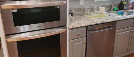 A kitchen with stainless steel appliances, white cabinetry, a granite countertop, and a window with a view of greenery.