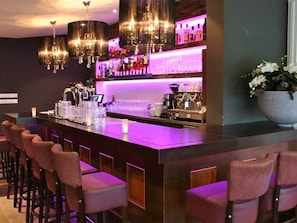 A bar area with a long counter, multiple bar stools, and a chandelier.