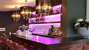 A bar area with a long counter, multiple bar stools, and a chandelier.