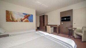 A hotel room with a large bed, a desk, a chair, a television, and a painting on the wall.