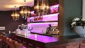 Una zona de bar con una barra larga, varios taburetes y una lámpara de araña.