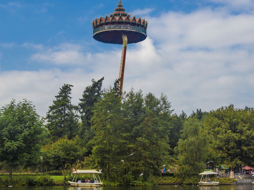 A tower with a traditional design, surrounded by lush greenery and a body of water with boats.