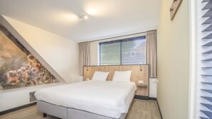 A bedroom with a bed, a window with blinds, a wooden headboard, and a wall with a decorative mural.