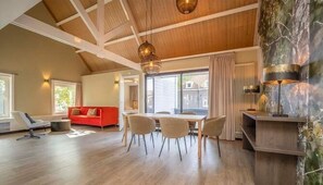 Amplia sala de estar con techo alto, vigas de madera, una mesa de comedor con sillas, un sofá rojo y una chimenea con lámparas decorativas.