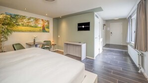 Ein Hotelzimmer mit einem großen Bett, einem Schreibtisch, einem Sessel, einem Fernseher und einem Landschaftsbild.
