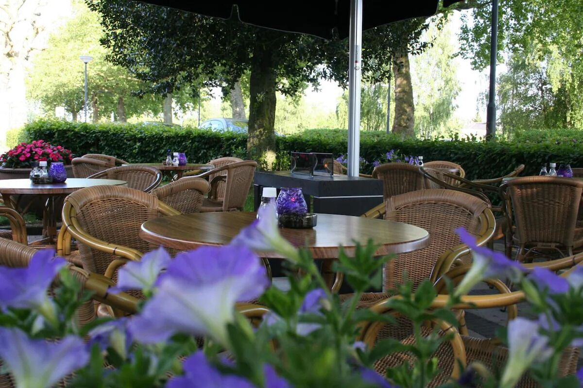 An outdoor seating area with wicker furniture and tables, surrounded by greenery and flowers.
