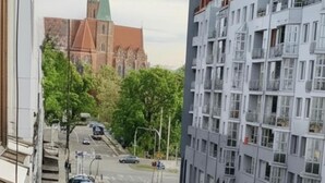 A view of a street with a church in the background, modern apartment buildings, and parked cars. - Charming studio with balcony near Ostrów Tumski Cathedral Island - Old Town in 15 min (Breslau)