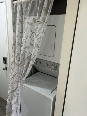 A compact, white laundry room with a front-loading washer and dryer, a door with a curtain, and a visible control panel. - Bayside Beauty- Walk to the Beach
Cozy 1-bedroom condo in charming Ocean City (Ocean City)