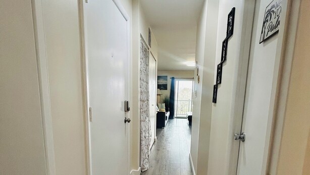 Un pasillo con piso de madera, paredes blancas y puertas que dan a otras habitaciones.
