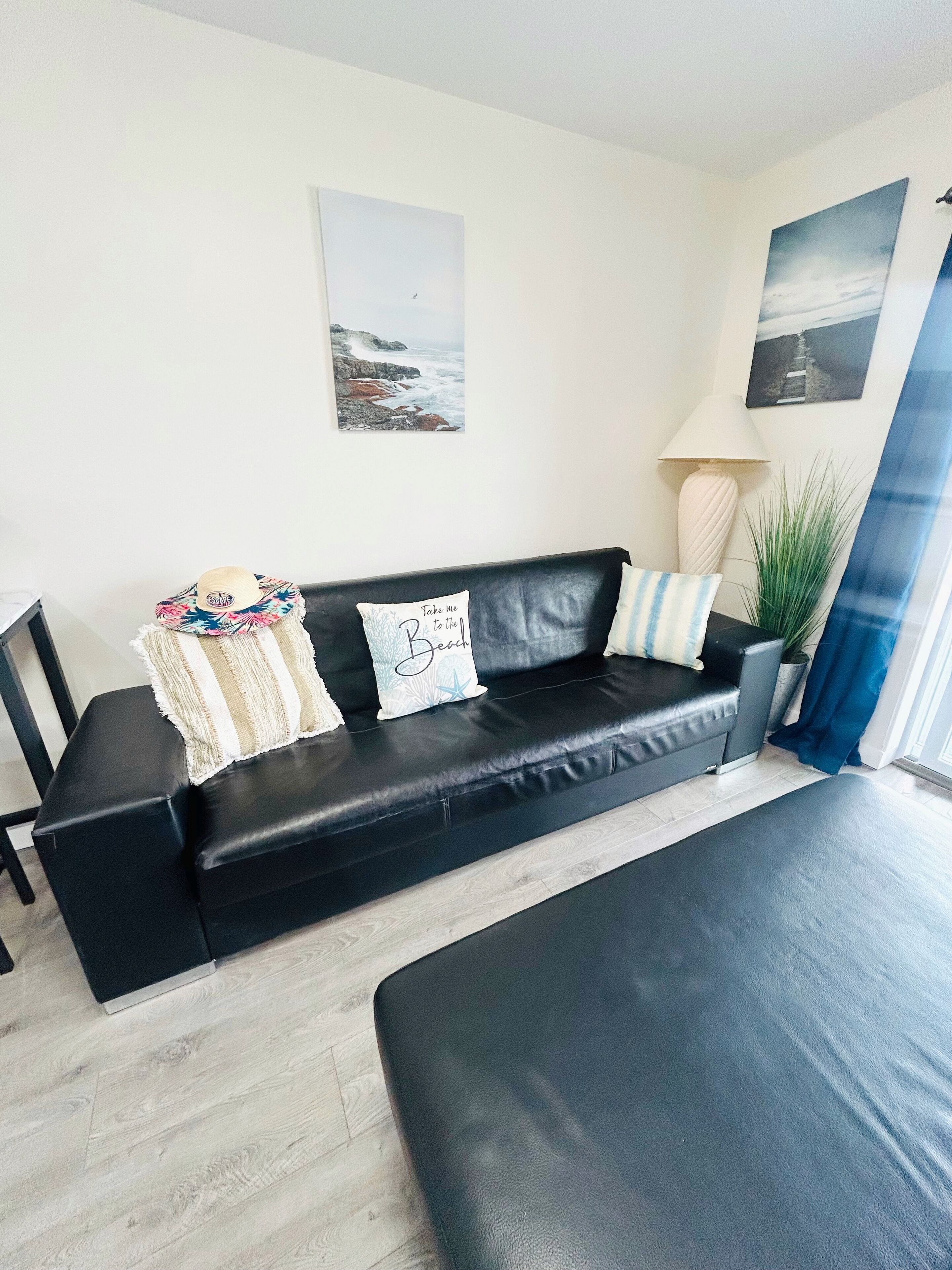 Een moderne woonkamer met een zwarte leren bank, een klein bijzettafeltje en een groot raam met uitzicht op zee.